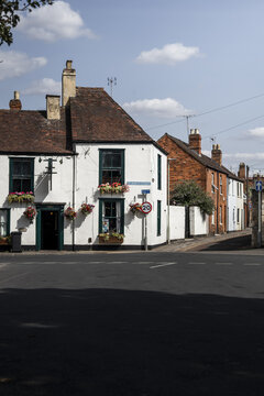 View of a historic white building with green window frames and flower boxes on St. Mary's Street, with a speed limit sign and brick buildings in Gloucester, England, United Kingdom.