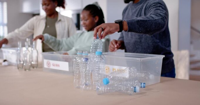 Family at kitchen table prompted by bottle pile, sorting into PLASTIC and GLASS bins, guiding child