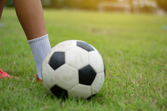 Close-up of a soccer player's ankle and leg on the grass field, preparing to control a football with a blurred ball background.