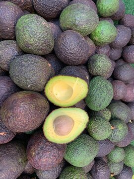 Avocado Bounty: A fresh pile of ripe avocados, one cut in half revealing its creamy green flesh and large pit, promises delicious culinary possibilities.