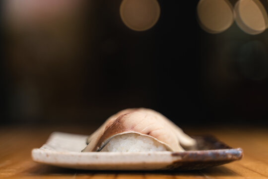 Two pieces of saba (mackerel)  sushis placed on a rustic ceramic plate, captured with a blurred and dramatic background.