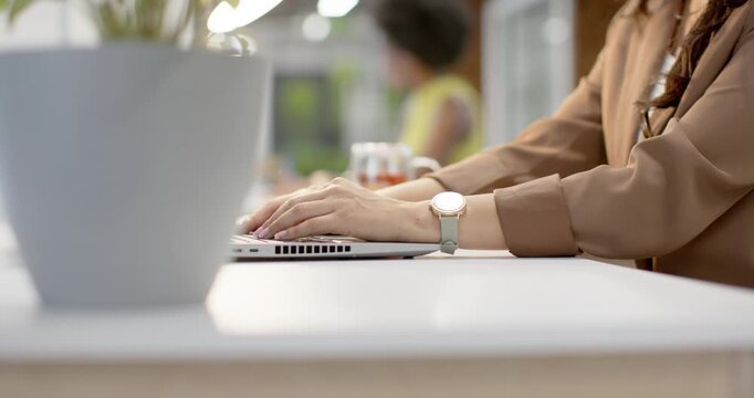 Diverse coworkers, African American woman resuming typing on laptop, watch visible, plant blurred