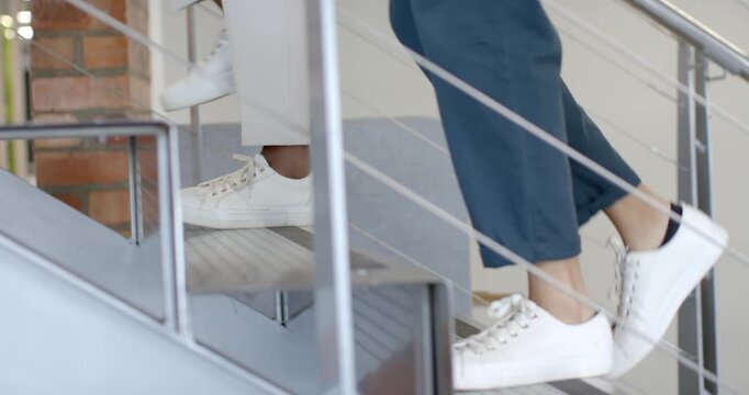 Placing leading feet on first risers, coworkers are climbing stairs in office to reach upper level