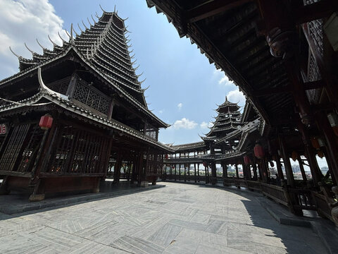 View of the traditional wooden Wanhe Drum Tower with its intricate multi-tiered roof and red lanterns, set against a clear blue sky in Huai Hua Shi, Hunan, China.
