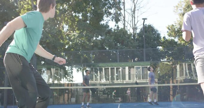 Four men blue court reacting to yellow return, left in teal stepping swinging paddle, copy space