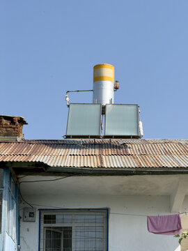View of a solar water heater system mounted on a corrugated metal roof against a clear blue sky in Posof, Ardahan, Turkiye.