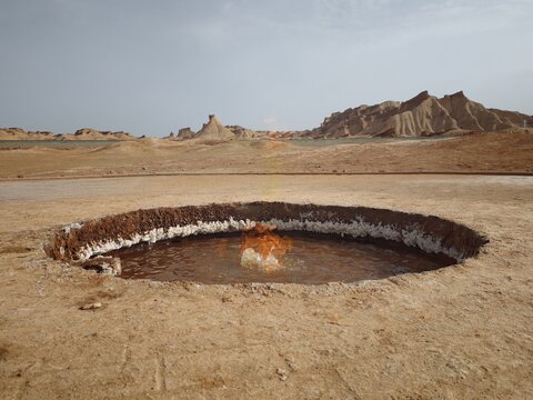 View of the natural gas fire burning in a circular pit within the arid desert landscape of Kezierxiang, Aksu Prefecture, Xinjiang, China.