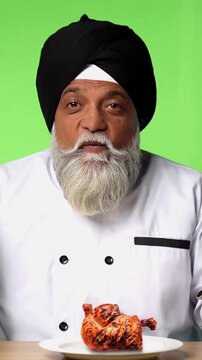 Indian Senior Male Sikh Chef in Traditional Attire Sitting at Table, Pointing at Empty Plate and Showing OK Sign on Green Screen