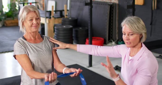 Senior female trainee holding blue band; trainer reaching shoulder, guiding chin tuck in gym