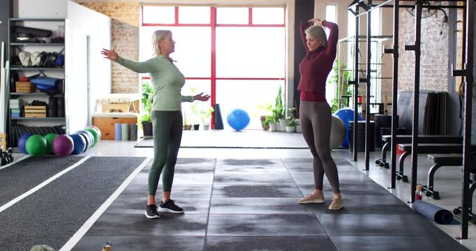 Senior women warming up from hands-behind-heads, mirroring shoulder stretches in sportswear on mat