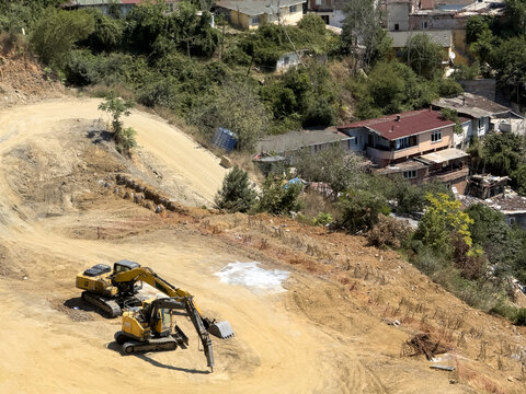 View of two yellow excavators working on a dirt slope at a construction site with residential houses in the background in Istanbul, Istanbul, Turkiye.