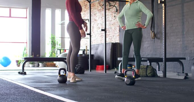 Two female partners coaching technique in gymwear while camera pulling back to kettlebells in gym