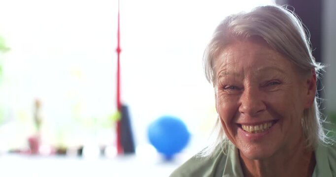 Senior woman smiling responding to off-camera voice at window with ball in green blouse, copy space