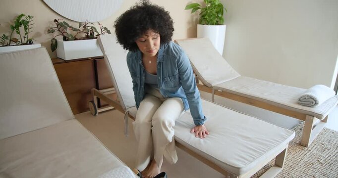 African American adult woman sitting on spa chaise removing shoes swinging legs reclining relaxing
