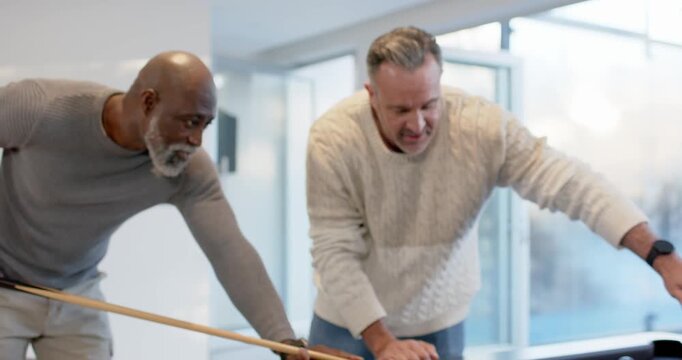 Diverse male friends leaning over black felt pool table with cue, one pointing, aiming for pocket