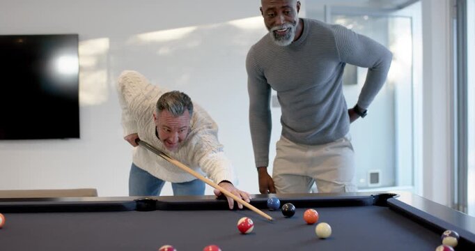 Diverse male friends after banter, lining up, striking balls with cues in game-room on black table