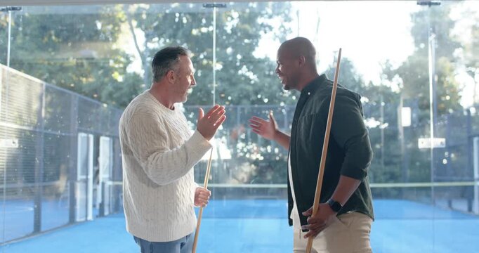 Diverse friends greeting after man entering right, gathering near glass wall holding cues playing