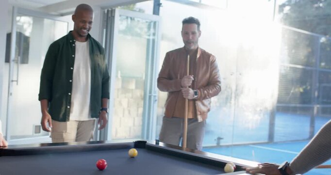 Diverse male friends playing pool, man in gray sweater moving in, lining up cue, taking shot