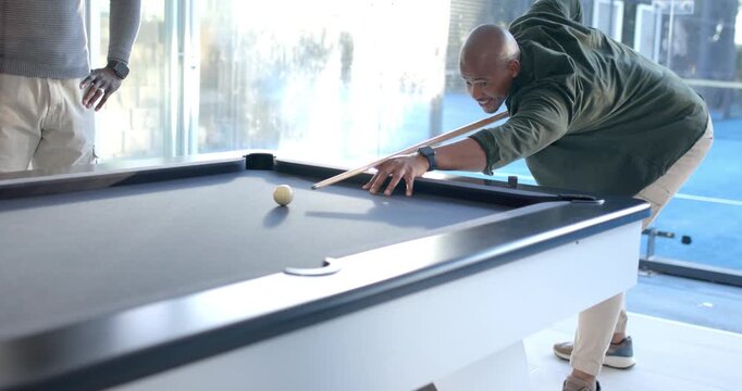 Mature African American man leaning over pool table, aiming, striking cue ball to break, copy space