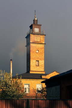Historic brick tower illuminated by evening sunlight beneath dramatic gray stormy sky