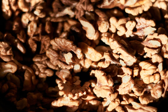 Warm sunlight illuminates a textured pile of chopped walnut pieces photographed closely.