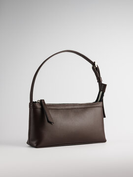 Elegant dark brown leather baguette shoulder bag on plain studio background