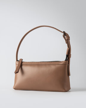 Minimalist light brown leather baguette shoulder bag on plain grey background