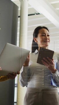 Animation of globe, graphs, loading bars and circles, diverse female coworkers discussing in office