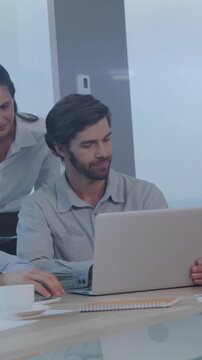 Animation of screens of mosaic squares over diverse colleagues discussing over laptop at office
