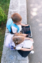 Top view of brother and sister with backpacks using a tablet and notebooks outdoors, highlighting modern education and digital learning. © Angelika Smile