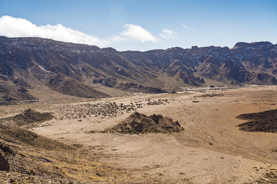 View of Mount Teide volcanic landscape with arid plains, rocky terrain, and distant mountain ridges under a clear blue sky in Santa Cruz de Tenerife, Canary Islands, Spain.