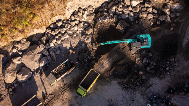 Aerial view of an excavator loading rocks into a dump truck at a mining quarry with workers nearby in Indonesia