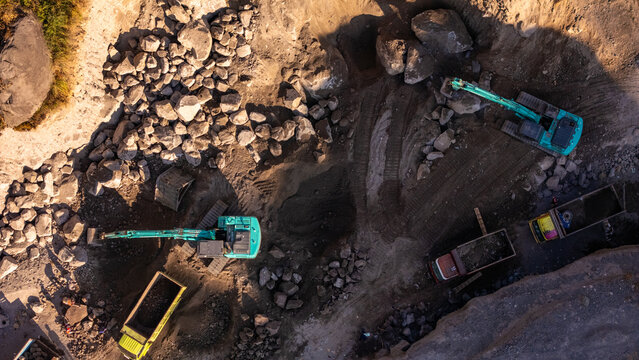Aerial view of an excavator loading rocks into a dump truck at a mining quarry with workers nearby in Indonesia
