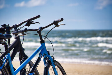 Fototapeta premium Blue Bicycles Parked on Sunny Sandy Beach With Ocean Waves and Summer Cycling Vibes