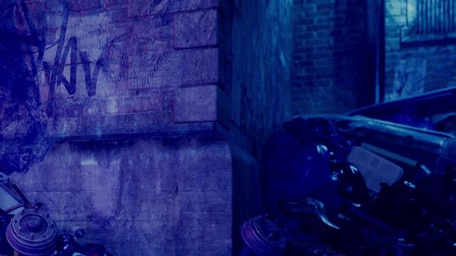 In a city area at night, graffiti covers a wall beside two parked motorcycles. The scene shows urban life with dim lighting and shadows creating a moody atmosphere.