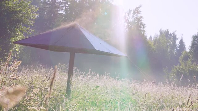 Rusty metal umbrella shelter in sunlit meadow with vertical sunbeam and pastel lens flare