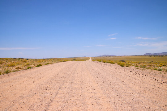 Eine lange Schotterstra&szlig;e verl&auml;uft gerade durch eine offene trockene Ebene im Brandberg in Namibia.