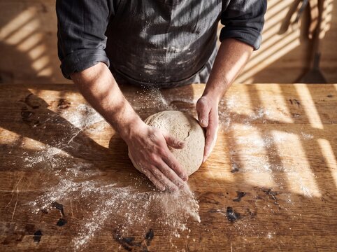 Artisan baker shaping fresh sourdough bread dough on a wooden table in sunlight