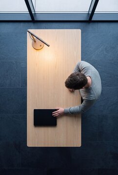 Overhead view of a businessman working at a minimalist wooden desk with a lamp in a modern office space