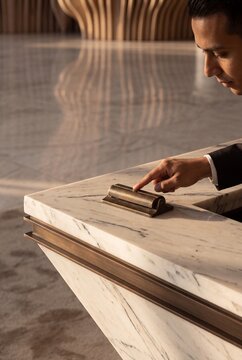 A businessman or hotel guest ringing a vintage brass service bell on a luxury marble reception desk