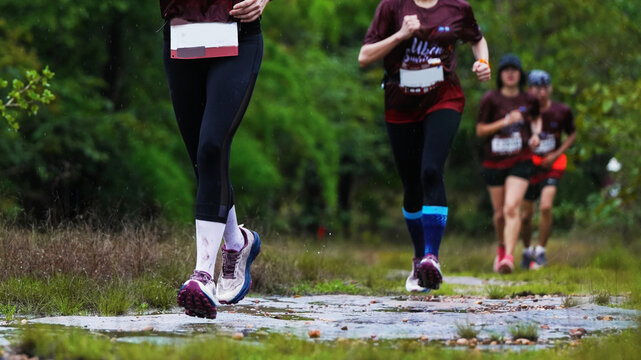 Trail runners racing together on a wet forest path during a rainy outdoor endurance event