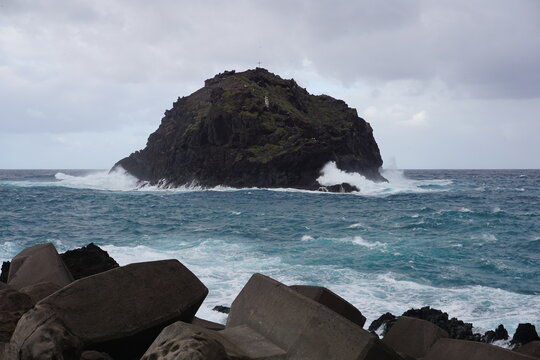 Rocky sea stack with crashing waves under stormy sky