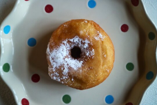 A classic traditional doughnut dusted with powdered sugar (snow doughnut) is served on a polka-dot ceramic plate.