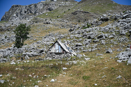Traditional stone and wood katun shepherd hut on the mountain. Rustic alpine shepherd cabin in the highlands. Traditional mountain stone hut and pasture landscape.