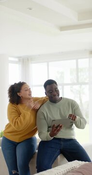 Vertical video: African American couple on bench, woman leaning man tapping tablet, sharing smiles