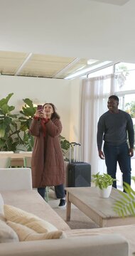 Vertical video: Couple entering living room, inspecting, she filming on phone while he moving case
