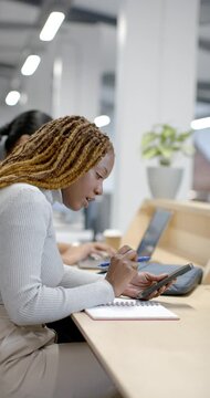 Vertical video: Diverse coworkers, African woman tapping tablet and noting in notebook at office