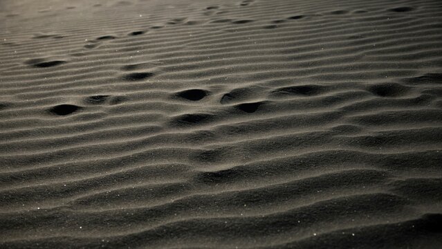 Close-up view of dark black volcanic sand dunes with visible human footprints and natural wind-blown ripple patterns on the surface