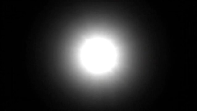 A brilliant, intense white circular light source glowing brightly against a completely dark, black background.