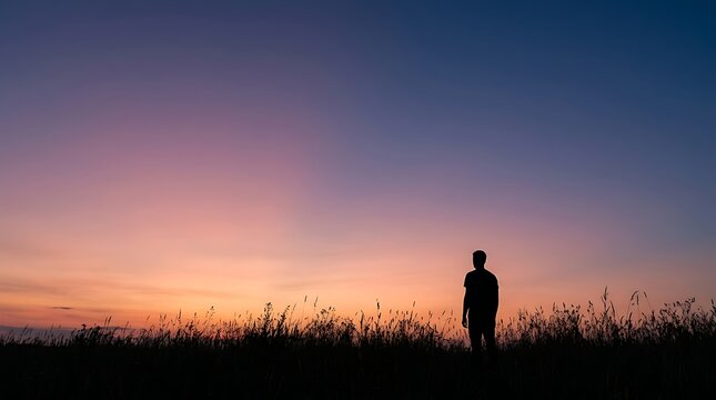 Man silhouette standing alone in a meadow under a colorful sunset sky
